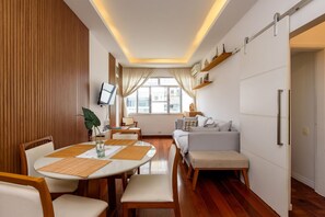 Uma sala de estar moderna com área de jantar, piso de madeira e uma janela grande.