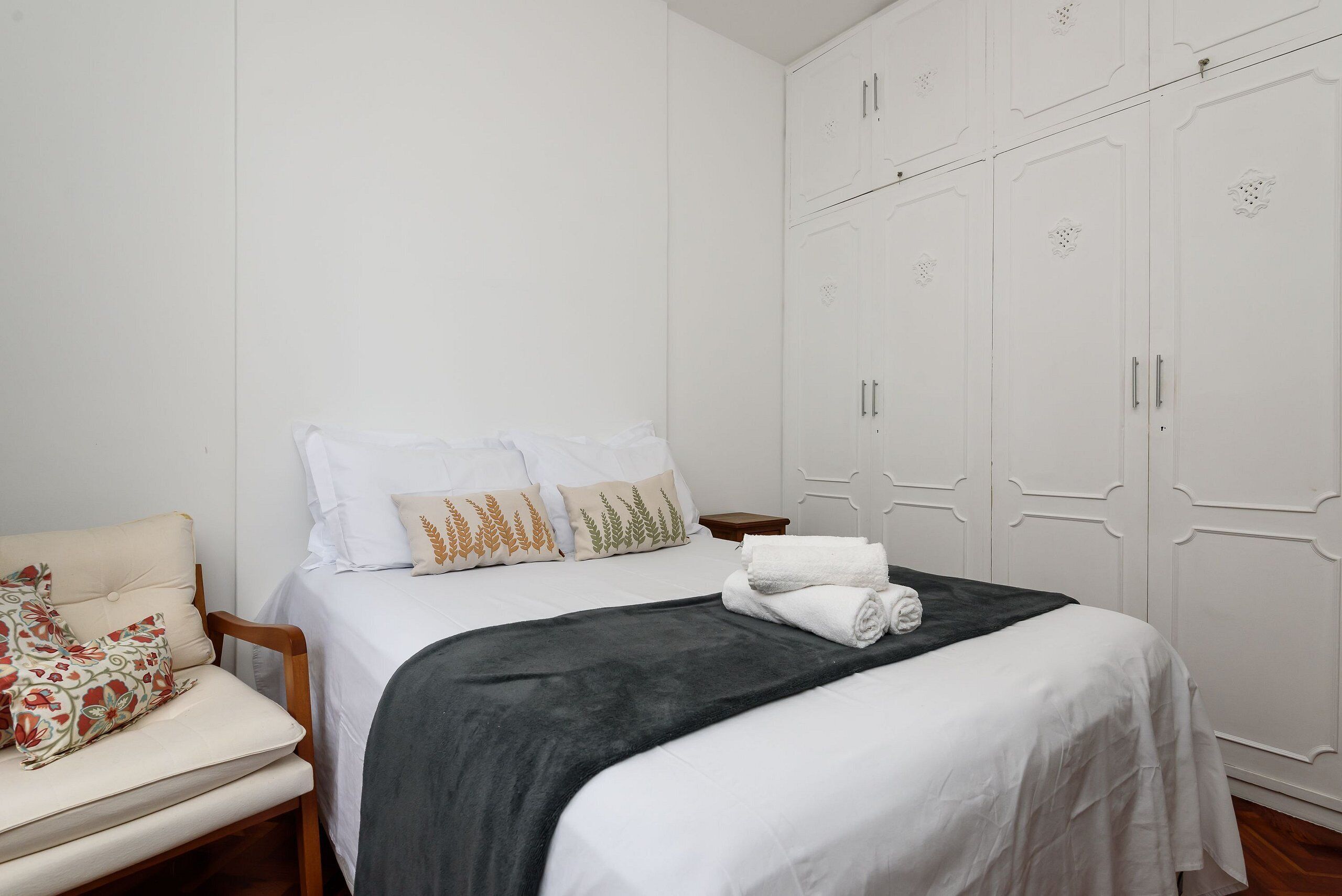 Un dormitorio con cama, una silla, un armario y una mesita de noche.