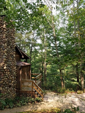 A rustic cabin with a stone exterior, wooden deck, and a staircase leading to a wooden door. - Old Man's Haven - Cabin 3 (Logan)