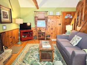 Una sala de estar acogedora con televisor, mueble de entretenimiento rojo, paredes de madera y un sofá gris.