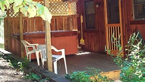 Eine Holzterrasse mit Whirlpool, zwei weißen Plastikstühlen und einem Holzzaun.