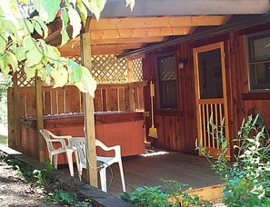 Una terraza de madera con un jacuzzi, dos sillas de plástico blanco y una valla de madera.