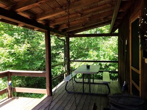 A wooden deck with a picnic table and a broom leaning against the wall. - Old Man's Haven - Cabin 1 (Logan)