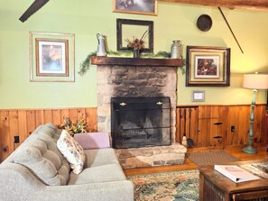 Una sala de estar acogedora con chimenea de piedra, paneles de madera, un sofá con cojines y una mesa de centro.