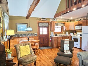 Una cocina acogedora con armarios de madera, un comedor con mesa y sillas, y una sala de estar con un sillón de cuero y un sofá.