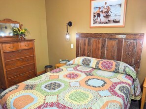 Un dormitorio con un aparador de madera, colcha acolchada, un cuadro en la pared y una mesita con una escultura de pez.