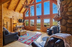 A log cabin interior with a large window, wooden walls, a fireplace, and a stone wall. - Mountain View Log Cabin w Hot Tub & Foosball (Bryson City)