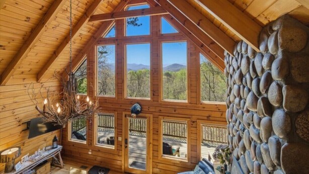 Una baita di legno con parete in pietra, ampie finestre e soffitto in legno.