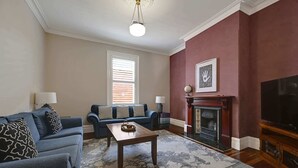 Een woonkamer met een blauwe bank, een houten salontafel, een open haard en een televisie.