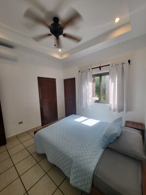 Une chambre à coucher avec un lit, un ventilateur de plafond et une fenêtre avec des rideaux.