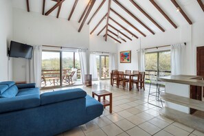 Un vaste espace de vie comprenant un canapé bleu, une table à manger en bois et un téléviseur fixé au mur.