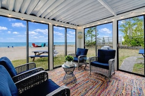 Ein überdachter Außenbereich mit Korbmöbeln, einem farbenfrohen Teppich und Blick auf den Strand.