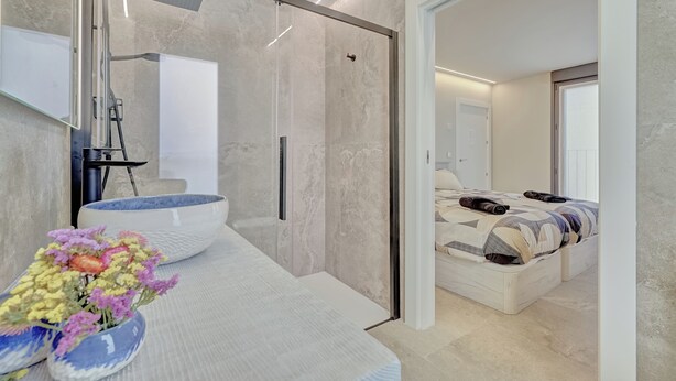 A modern bathroom with a large mirror, a white sink, and a shower area. There is a bed with a patterned bedspread in the adjacent room. - LA FRAGUA ANCÍN APARTMENT (Ancín)