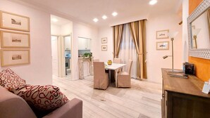 Un salon moderne avec un canapé, une table à manger et des chaises, une cuisine en arrière-plan et un grand miroir au mur.