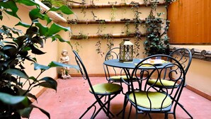 Une terrasse avec une table ronde et des chaises, entourée de plantes en pot et d’une statue.