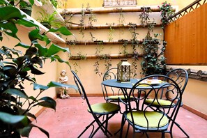 Eine Terrasse mit rundem Tisch und Stühlen, umgeben von Topfpflanzen und einer Statue.