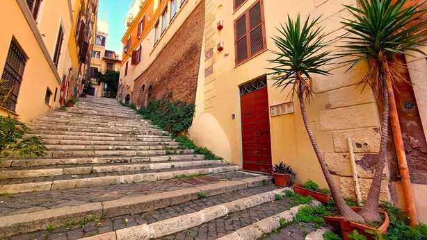 Une ruelle étroite avec des marches en pierre menant à un bâtiment doté d’une porte rouge.