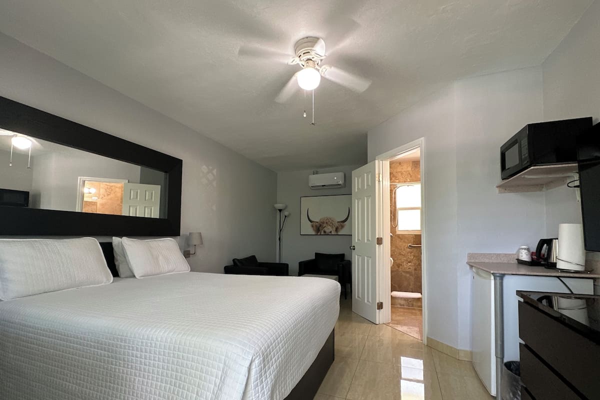 Ein Hotelzimmer mit einem großen Bett, einem Deckenventilator, einem Schreibtisch mit einer Mikrowelle und einem durch eine geöffnete Tür einsehbaren Badezimmer.