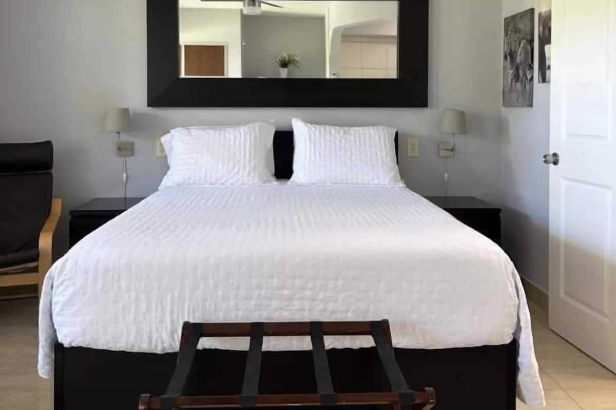 Ein modernes Schlafzimmer mit einem großen Bett, einer hölzernen Bank, einem Deckenventilator und einem Spiegel an der Wand.