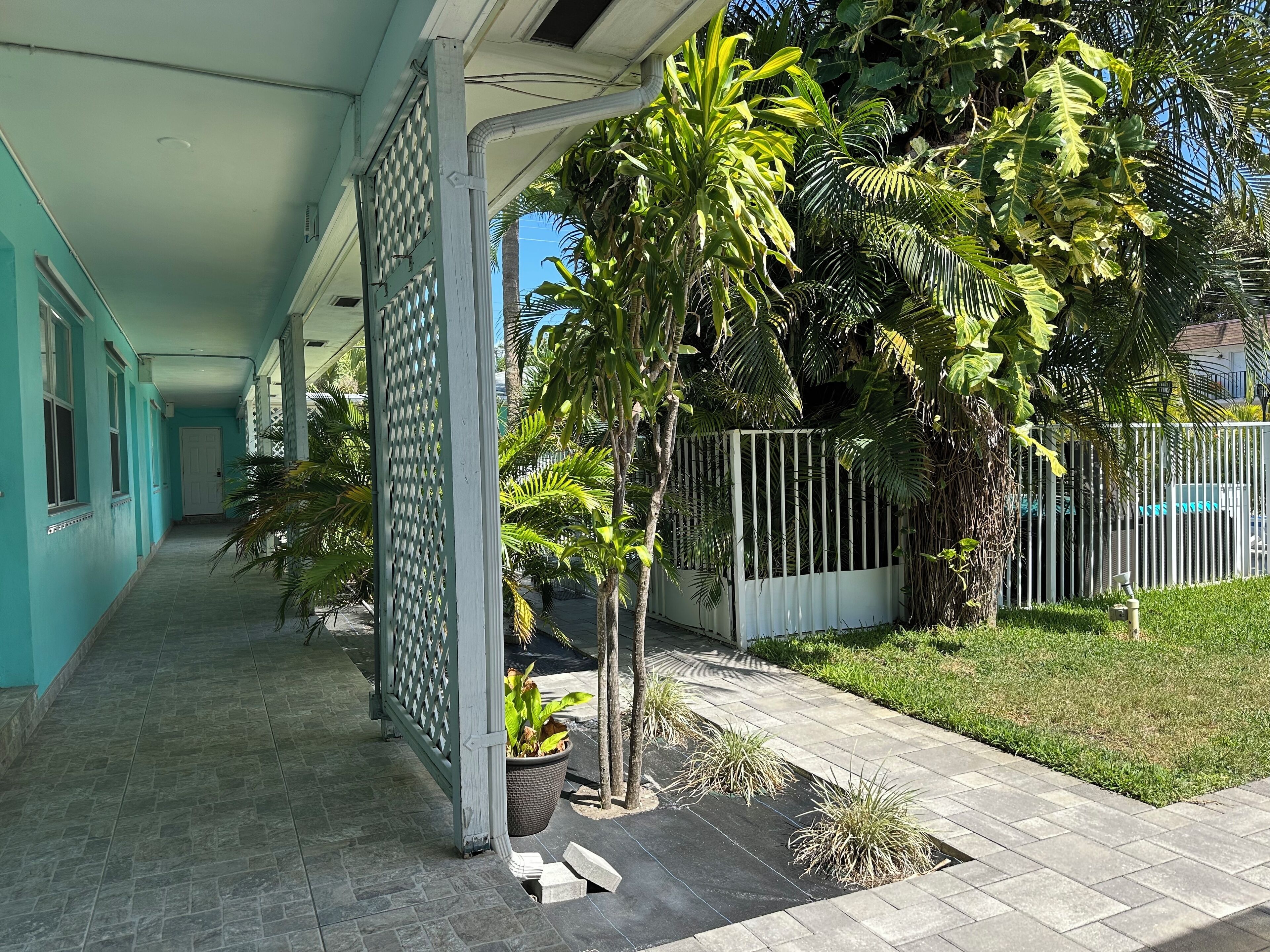 A covered walkway with a tiled floor, a metal fence, and various potted plants.