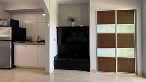 Eine moderne Küche mit weißen Schränken, einem schwarzen Kühlschrank und einem eingebauten Backofen. Es gibt eine schwarze Unterhaltungseinheit mit einer Pflanze darauf.