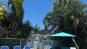 Ein Poolbereich mit Liegestühlen, einer überdachten Sitzgelegenheit und einem Pool mit einem 'Nicht springen'-Schild.