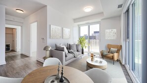 Ett modernt vardagsrum med en grå soffa, ett runt soffbord och utsikt över staden genom stora fönster.
