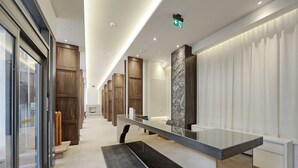 En modern hotellobby med en receptionsdisk, trädörrar, en accentvägg i sten och en glasvägg.