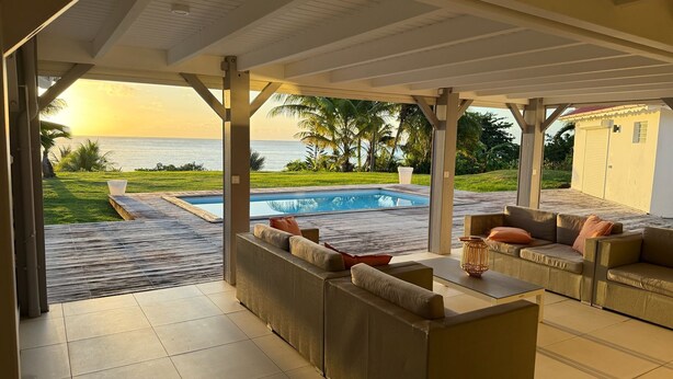 A covered outdoor seating area with a pool, a view of the ocean, and a well-maintained lawn.