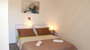 Cama bem arrumada com roupa de cama marrom e branca, duas luminárias de cabeceira e um quadro pendurado acima da cama.