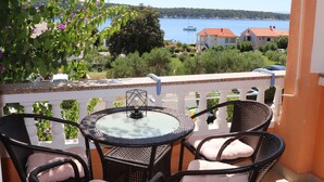 Varanda com mobiliário de vime e mesa de vidro, com vista para uma área costeira com casas e barcos.