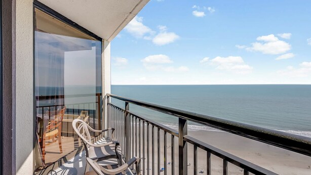 Ein Balkon mit Blick auf den Strand, ein Tisch mit Stühlen und eine Glastür.