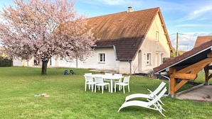A house with a sloped roof, a lawn with a table and chairs, and a tree with pink blossoms. - 3 bedroom amazing home in Mutigney (Mutigney)