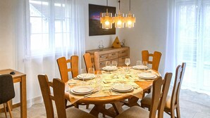 A dining room with a round table set for six, wooden chairs, a chandelier, and a wooden cabinet with drawers. - 3 bedroom amazing home in Mutigney (Mutigney)