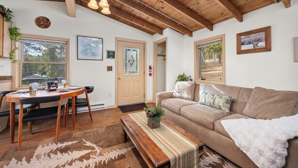 A cozy living room with a wooden ceiling, a brown sofa, a coffee table, and a dining area with a wooden table and chairs.