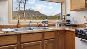 A kitchen with wooden cabinets, a double sink, a stove, and a window with a mountain view.