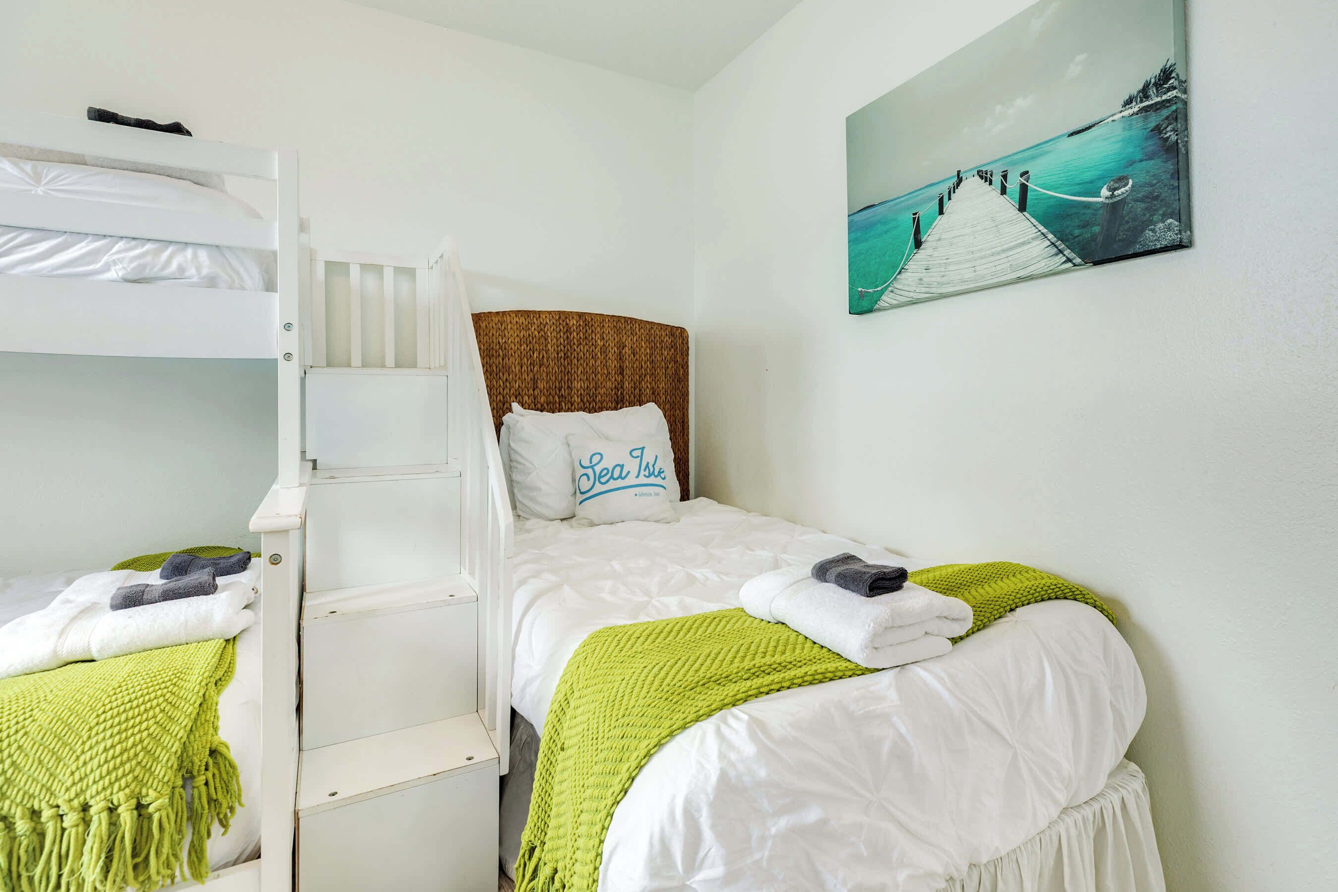 Una stanza con un letto a castello, un letto singolo e un quadro raffigurante un molo.