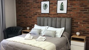 A bedroom with a brick wall, a grey upholstered headboard, a grey bedspread, two pillows with the word "inhale," a bedside table with a lamp, and a chair. - Puente de la Mujer, your private apartment with the best view in Bs. As. (Buenos Aires)