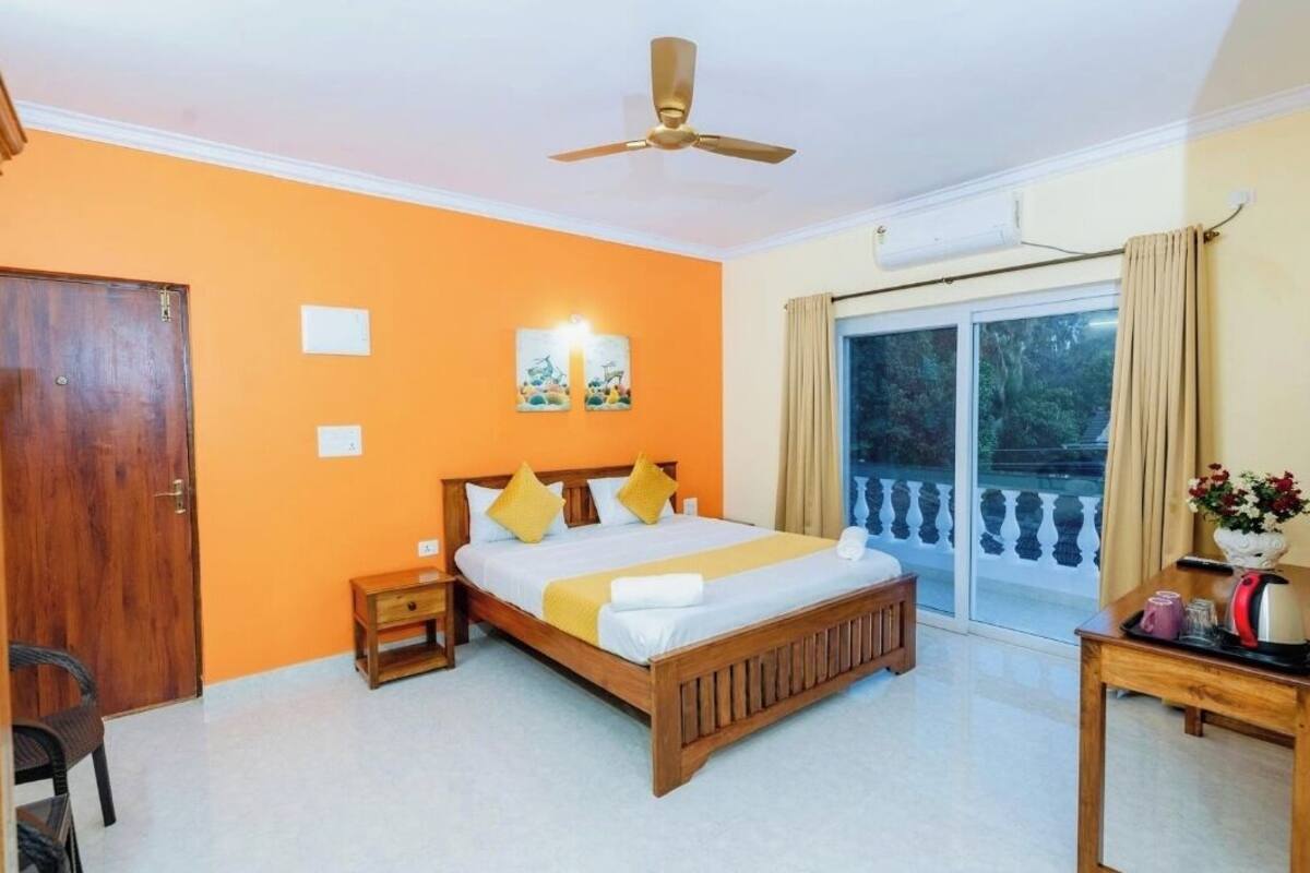 A bedroom with a bed, a nightstand, a wooden chair, a table with a vase, and a window with curtains.