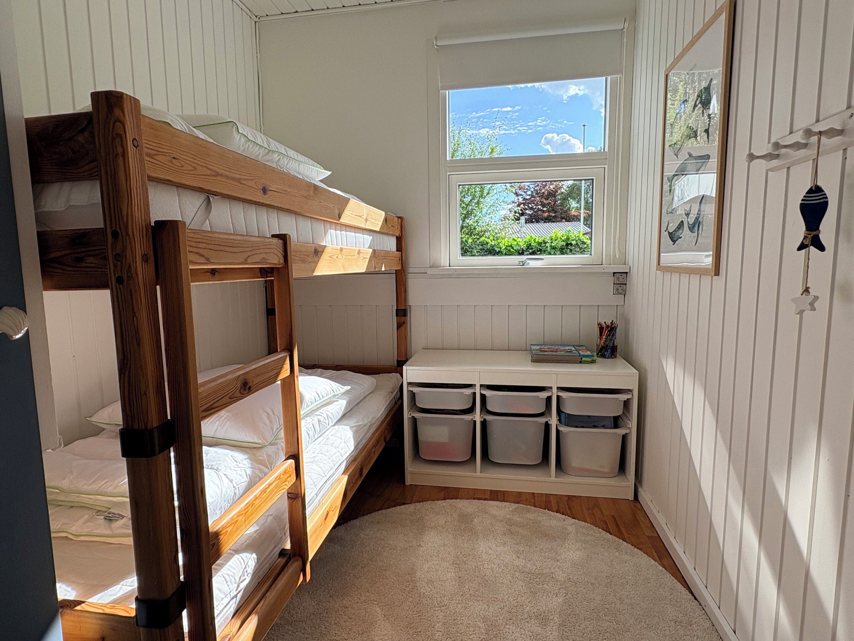 A bunk bed room with a window, storage bins, and a small desk.