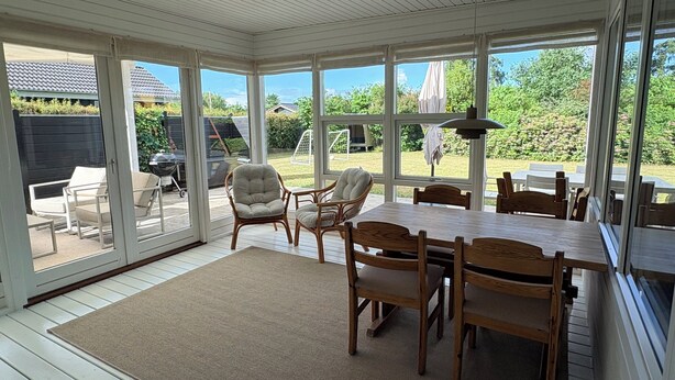 A sunroom with large windows, a wooden table, and wicker chairs. - A sanctuary by the water – Vejlby Fed (Middelfart)