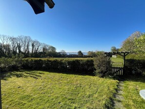 A grassy outdoor area with a pergola, a hedge, and a view of the sea.