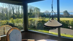 Une pièce dotée d’une grande fenêtre, d’un luminaire suspendu et de deux fauteuils en osier.
