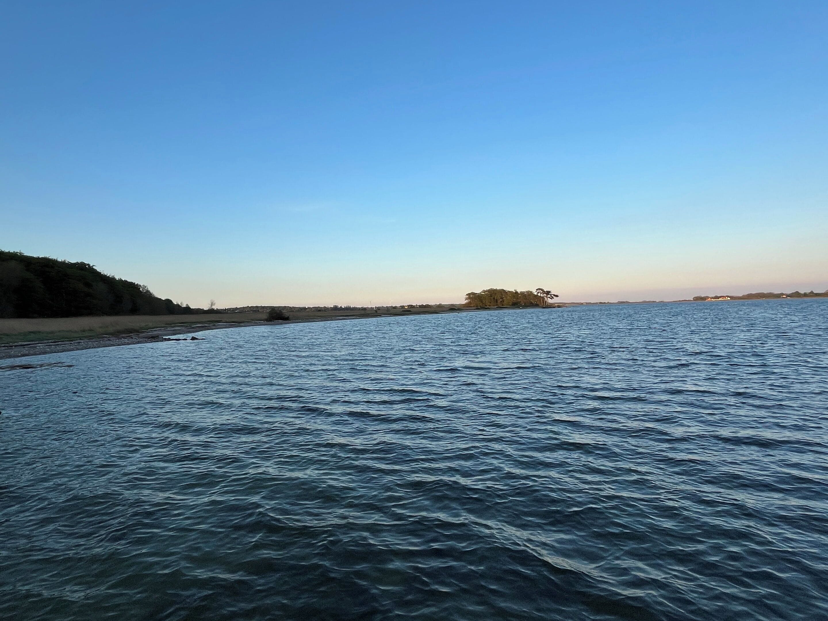 Een rustig wateroppervlak met een eiland in de verte en een oefer met bomen.