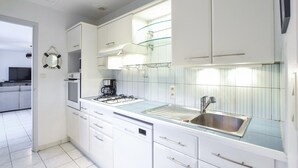 Una cocina moderna con armarios blancos, un lavamanos de acero inoxidable y un protector contra salpicaduras de vidrio.