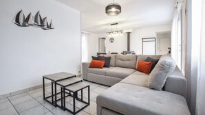 Una sala moderna con un sofá gris, una pequeña mesa de centro y un comedor al fondo.