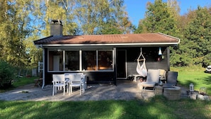 Ett litet hus med en veranda, en möblerad uteplats och en trädgård.