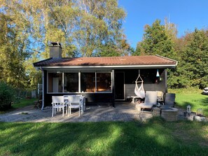 Ein kleines Haus mit einer Veranda, einer überdachten Sitzgelegenheit im Freien und einem Garten.