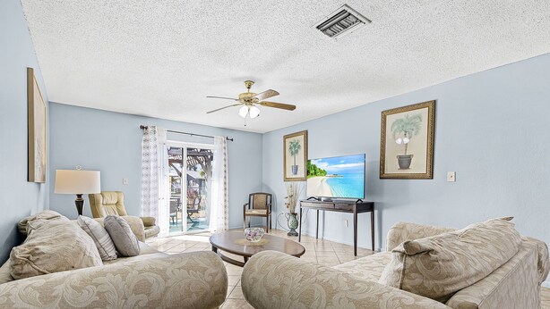 Ein Wohnzimmer mit Deckenventilator, zwei Sofas, einem Couchtisch, einem Fernseher und einer Tür zum Balkon.