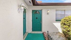 Ein Haus mit grüner Tür, weißen Wänden und einer kleinen Veranda mit einer grünen Fußmatte.